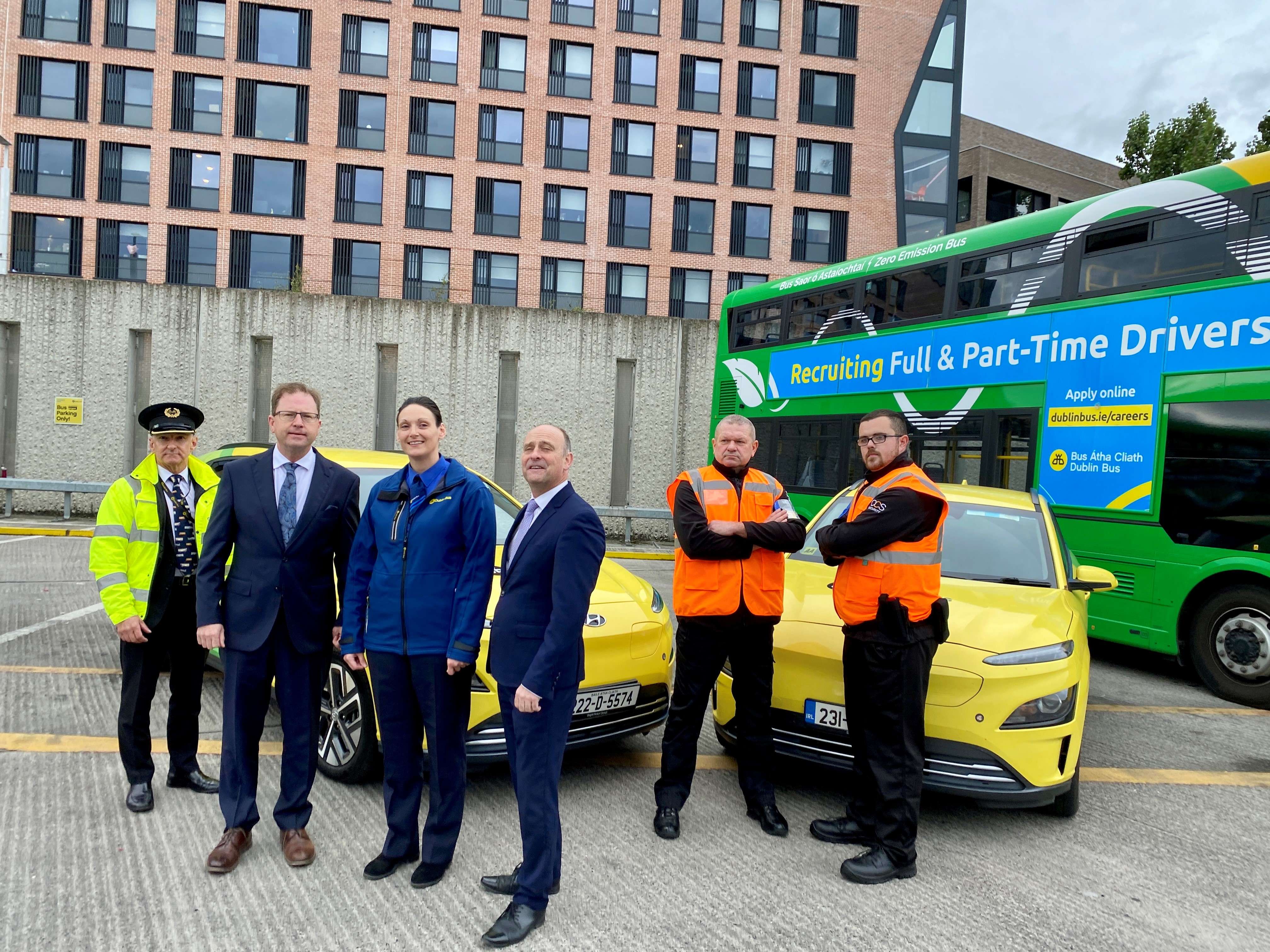 Dublin Bus employees standing by wrapped cars and a bus inside bus depot