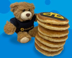 Image a teddy bear wearing a Dublin Bus tshirt and a stack of pancake with the Dublin Bus logo on them