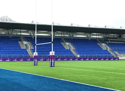 Image of side goal of Rugby pitch, green grass and blue stands.