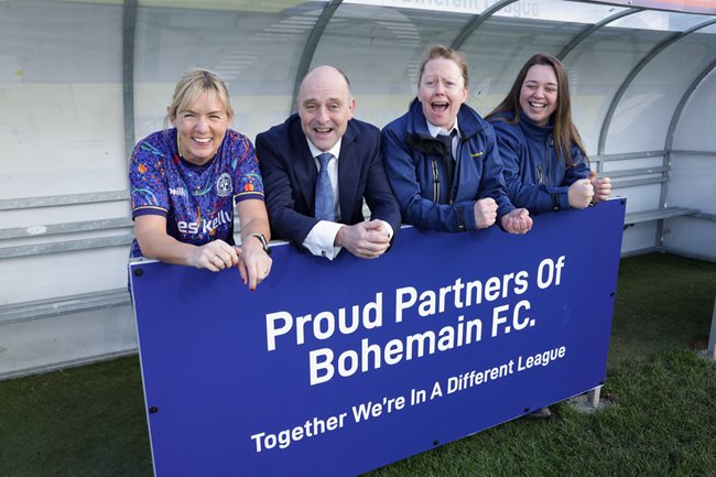 Image of three Dublin Bus employees and CEO of Dublin Bus Billy Hann behind billboard that reads 'Proud Partners of Bohemian FC, Together we are in a different league'