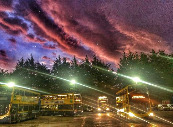 Instagram image of buses in the depot in the dark with bus lights on and the sun setting and red sky