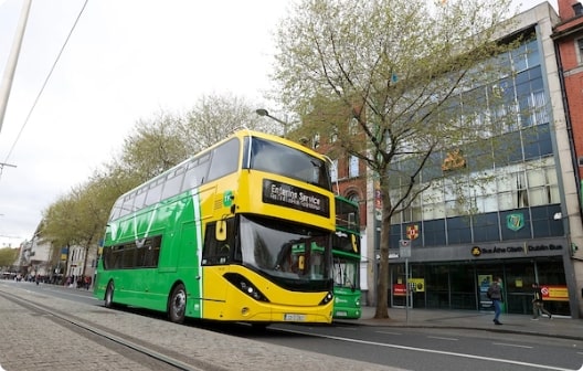 Parked double decker bus on O'Connell Street featuring Dublin Bus Head Office in the background